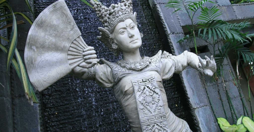 Intricate stone statue of a Balinese dancer with fan, set against a natural backdrop in Bandung, Indonesia.